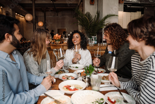 Group of cheerful friends talking and drinking wine while dining in restaurant