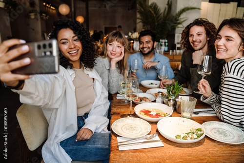 Group of cheerful friends taking selfie while dining in restaurant