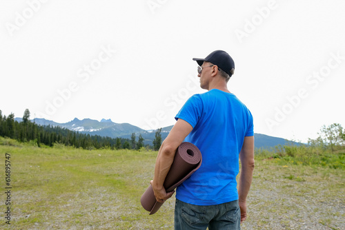 Men stand back with yoga mat in mountains landscape. Outdoor yoga in mountains