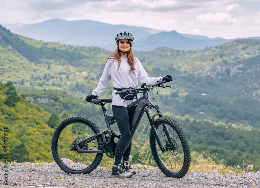 Fototapeta premium Happy girl wearing helmet and sportswear with her hightech electric bicycle on top of a canyon