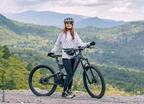 Happy girl wearing helmet and sportswear with her hightech electric bicycle on top of a canyon