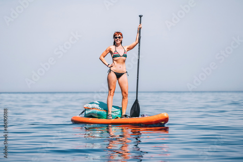 Happy gorgeous girl with a paddle swims on a sup board on the sea. Healthy lifestyle and recreation concept