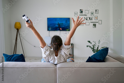 Happy woman winning in video game and sitting with arms raised at home photo