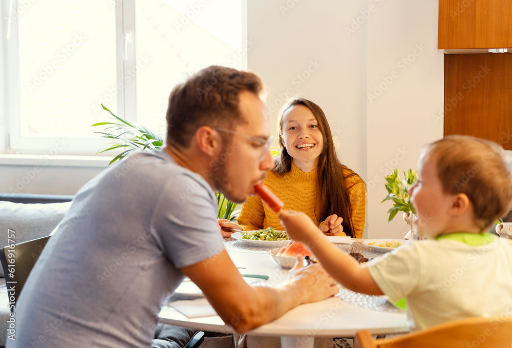 Smiling mother looking at boy sharing popsicle with father at dining table Smiling mother looking at boy sharing popsicle with father at dining table