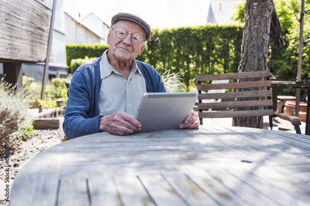 Smiling senior man sitting with tablet PC at table Smiling senior man sitting with tablet PC at table