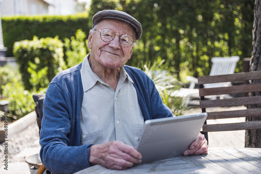 Smiling senior man sitting with tablet PC at table in back yard Smiling senior man sitting with tablet PC at table in back yard