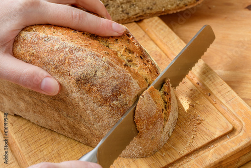 Bochenek chleba krojony nożem na drewnianej desce w kuchni