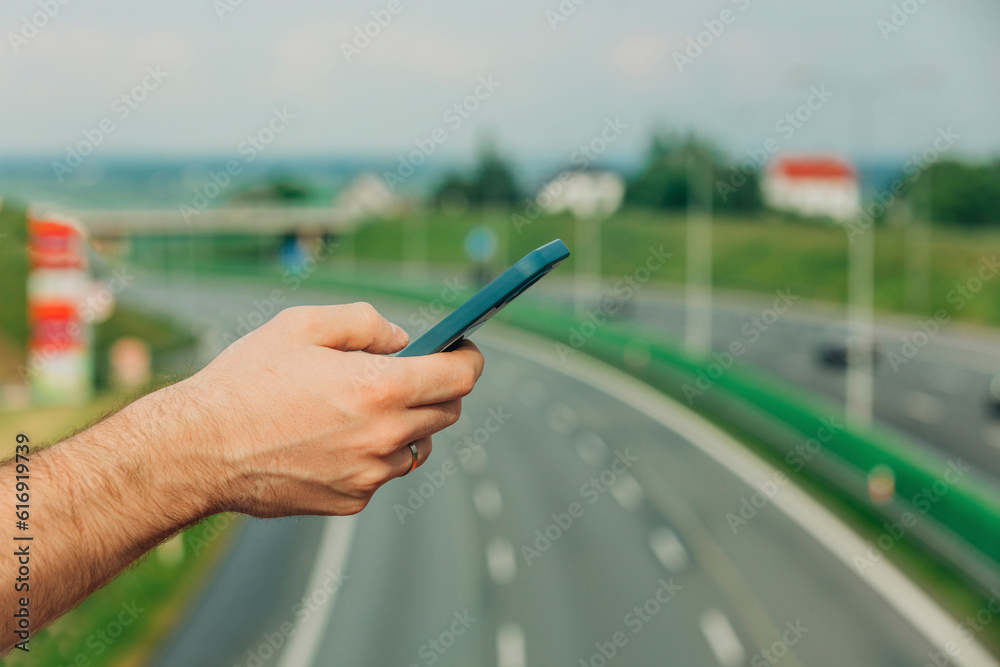 Hand of man surfing net through smart phone with highway in background Hand of man surfing net through smart phone with highway in background