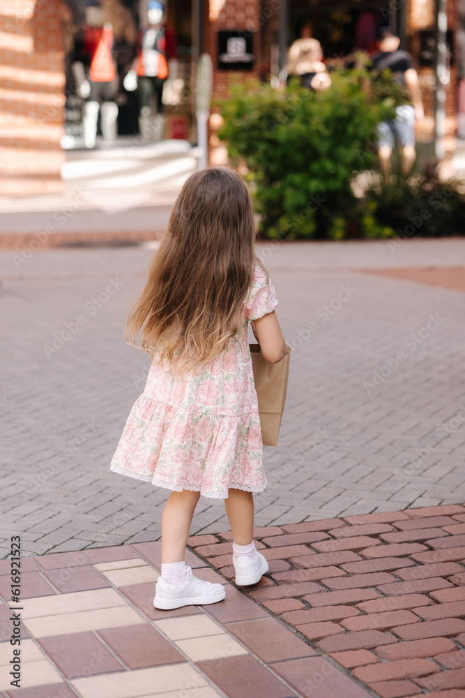 Back view of cute little girl on shopping. Portrait of adorable kid with shopping bags