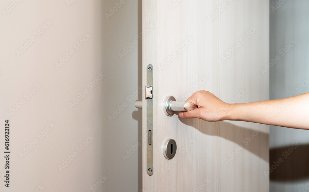 Female hand on door handle, opening the door. - obrazy, fototapety, plakaty 