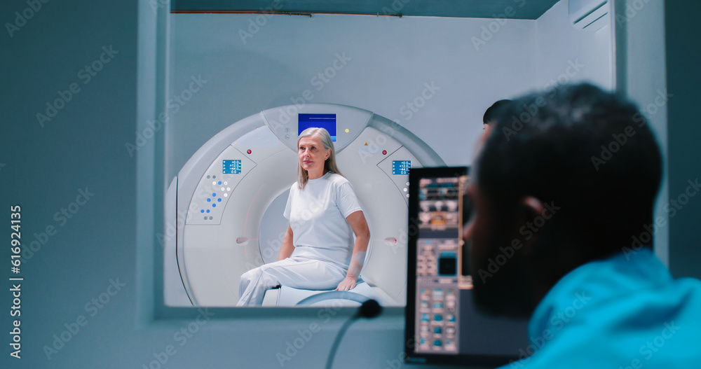 Elderly woman lies down in MRI capsule. Doctor monitors examination on