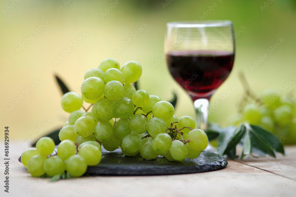 Frische weiße Weintrauben und ein Glas Rotwein auf dem Tisch Frische weiße Weintrauben und ein Glas Rotwein auf dem Tisch