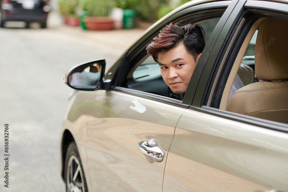 Young man looking back through window when parking in front of house
