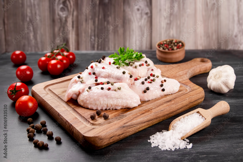 Raw chicken wings with ingredients for cooking on a wooden cutting board on a dark background. Raw chicken wings with ingredients for cooking on a wooden cutting board on a dark background.