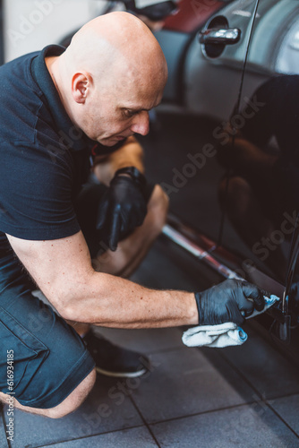 Service man washing car before detailing in workshop.