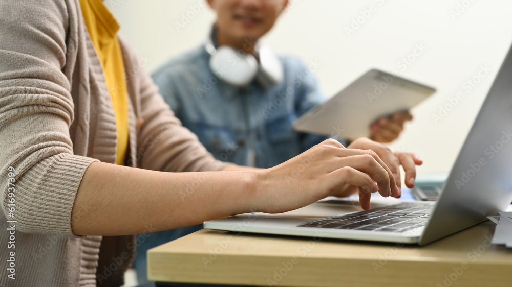 Side view of young creative woman hands typing on laptop keyboard, working on project with colleague in office Side view of young creative woman hands typing on laptop keyboard, working on project with colleague in office