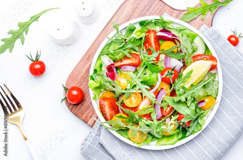 Fresh vegan vegetable salad with colorful tomatoes, cucumber, red onion, lettuce and arugula. White table background, top view