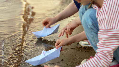 Close up of childrens hands play with paper boats on sea or river in summer at sunset. Kids outdoors by water