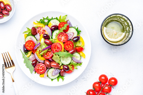 Vegan salad with kalamata olives, cherry tomato, yellow paprika, cucumber and red onion, tasty and healthy mediterranean food, low calories eating. White table background, top view