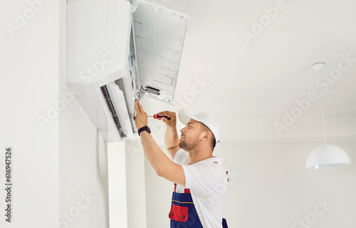 Worker installing a new modern air conditioning system. Young man in a uniform cap installing an air conditioner on a white wall in the house. AC installation, maintenance, repair service concept