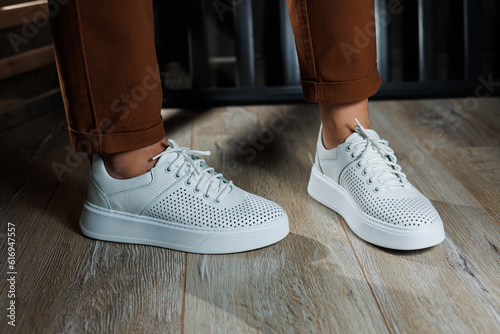 Slender female legs in pants close-up in white casual sneakers. Women's leather shoes.