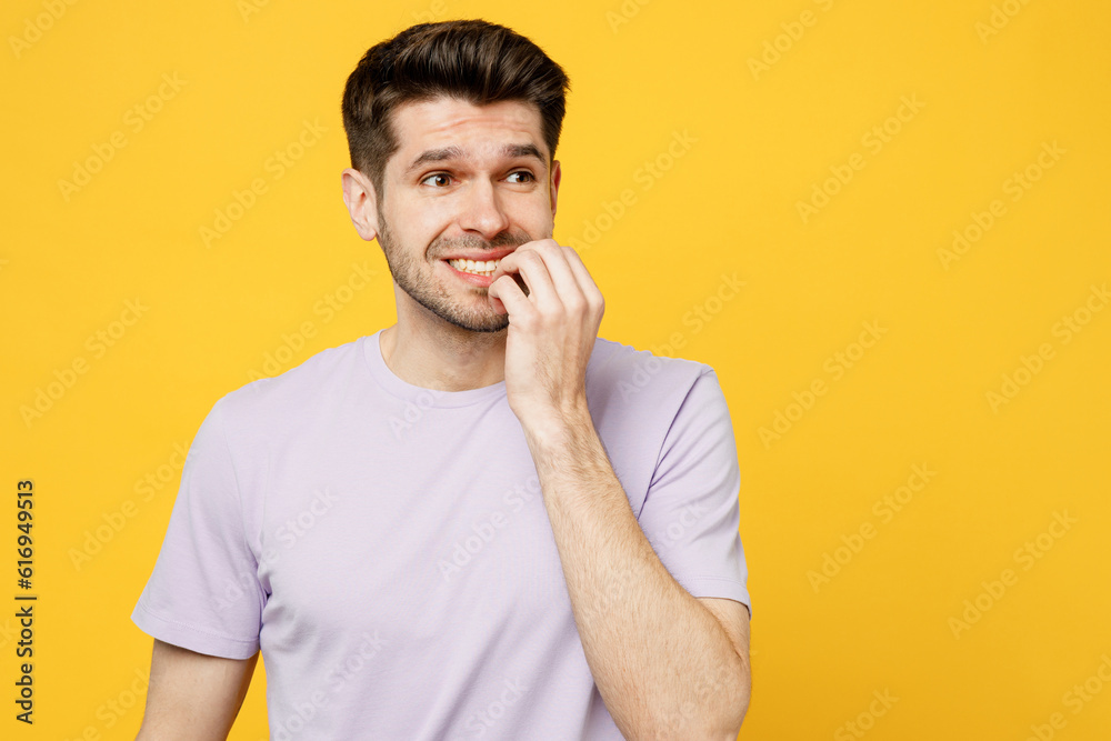 Young confused mistaken minded pensive sad caucasian man wear light purple t-shirt casual clothes look aside biting nails fingers isolated on plain yellow background studio portrait Lifestyle concept