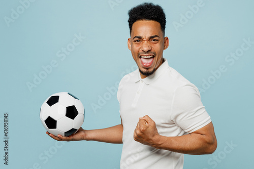 Side view happy young man fan wear basic t-shirt cheer up support football sport team hold in hand soccer ball watch tv live stream do winner gesture isolated on plain pastel blue background studio.