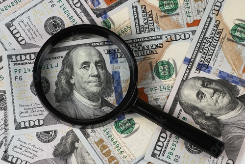 Magnifying glass on 100 dollar banknotes close up