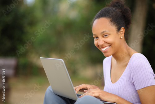 Happy black woman using laptop looking at you in a park © PheelingsMedia