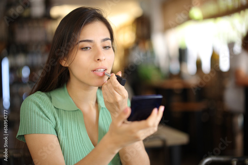 Woman painting lips before dating in a restaurant