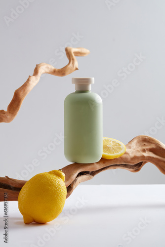 Scene for advertising product with lemon extract - fresh lemon decorated with green bottle unlabeled and dry twigs on white background. Lemons are rich in vitamin C, which improves skin