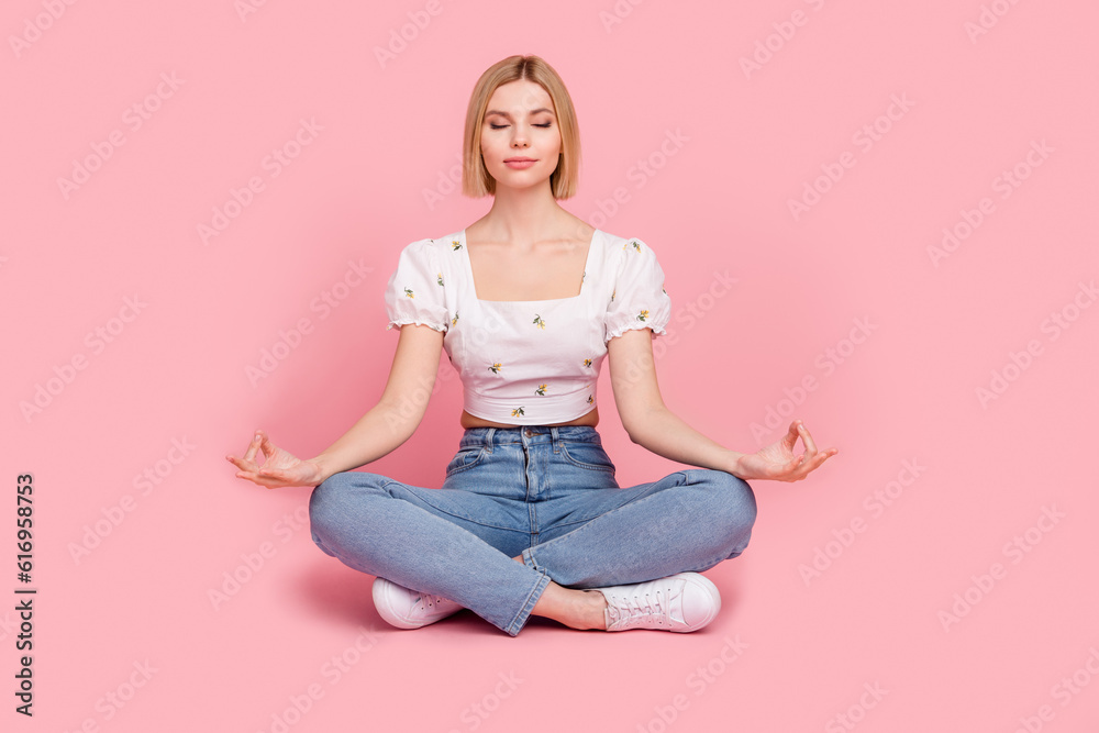 Full length cadre of young girl sitting crossed legs balance yoga meditation closed eyes practice retreat isolated on pink color background Full length cadre of young girl sitting crossed legs balance yoga meditation closed eyes practice retreat isolated on pink color background