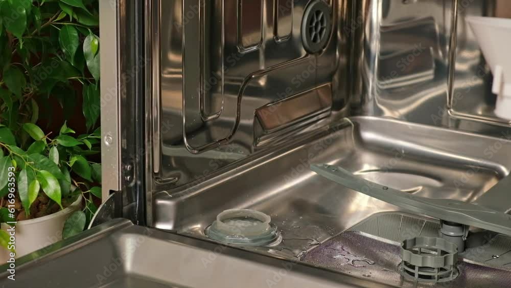 The man opens the salt compartment at the bottom of the dishwasher and pours salt into it