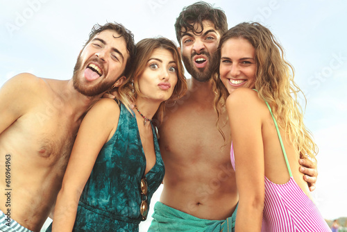 Joyful Young Friends Posing on Beach - Four happy, young friends in swimwear make faces at the camera, embodying the joy of a shared vacation.