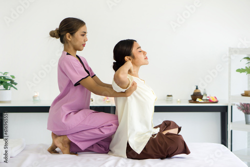 Cute girl with traditional dress stretch back and shoulder by massager. Young asian woman relax in spa. Body care treatment by thai massage performed Hermit exercise.