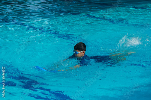 Image of lonely Asian young boy age 6-7 years old hold a kickboard to learning to use the legs for beginner swimming on butterfly position. Background for recreation or outdoor sport concept.
