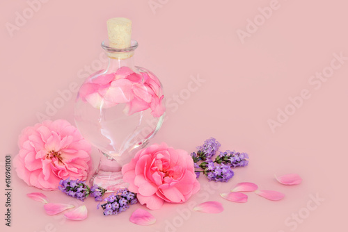 Rose and lavender flower perfume in heart shaped bottle on pink with loose flowers. Natural pure beauty floral product, gift for Valentines Day, birthday, anniversary or Mothers day.