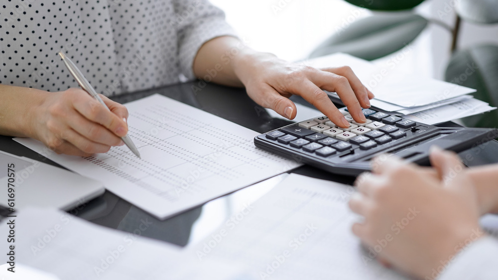 Woman accountant using a calculator and laptop computer while counting taxes with a client or a colleague. Business audit team, finance advisor Woman accountant using a calculator and laptop computer while counting taxes with a client or a colleague. Business audit team, finance advisor