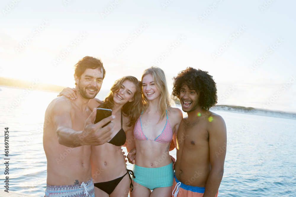 Young adult friends in bikinis swim trunks taking selfie at summer sunset ocean Young adult friends in bikinis swim trunks taking selfie at summer sunset ocean