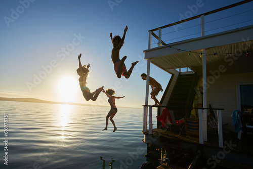 Young adult friends jumping off summer houseboat into sunset ocean photo