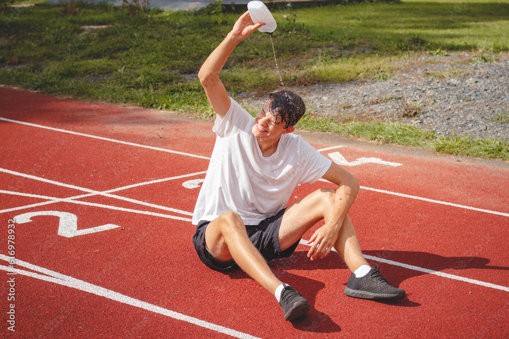 Obraz premium Young athlete refreshes himself with water after a hard workout on the athletic oval in the intense heat. Endurance training. Brown-haired adolescent