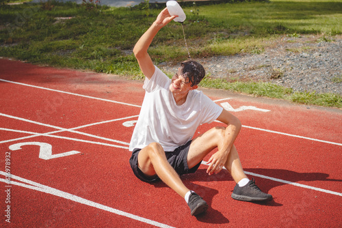 Young athlete refreshes himself with water after a hard workout on the athletic oval in the intense heat. Endurance training. Brown-haired adolescent