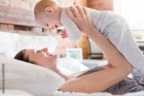 Smiling mother holding baby daughter overhead on bed