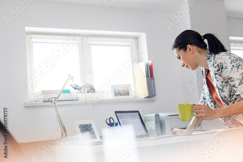 Businesswoman drinking coffee and working at laptop in office