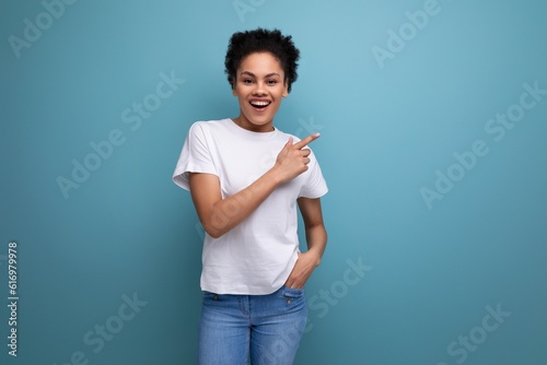 young brunette woman with afro hair in a white t-shirt shows her hands on an empty space for a mockup