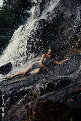 Young wet woman lying on rock near waterfall between water flows.