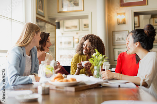 Smiling women drinking coffee and talking at restaurant table