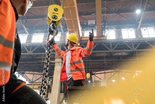 Картината върху платно Steel workers fastening chain to crane in factory
