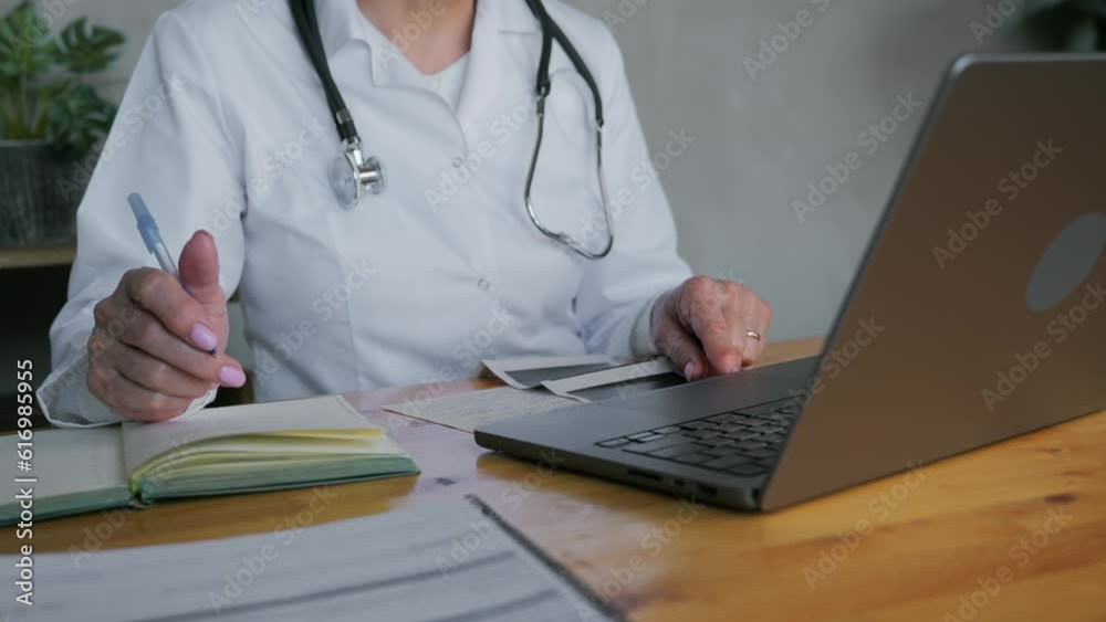 Close-up with the unrecognizable face of the chief doctor of a woman who is sitting and working at a desk in her office in a white coat. The doctor works with documents. High quality 4k footage Close-up with the unrecognizable face of the chief doctor of a woman who is sitting and working at a desk in her office in a white coat. The doctor works with documents. High quality 4k footage