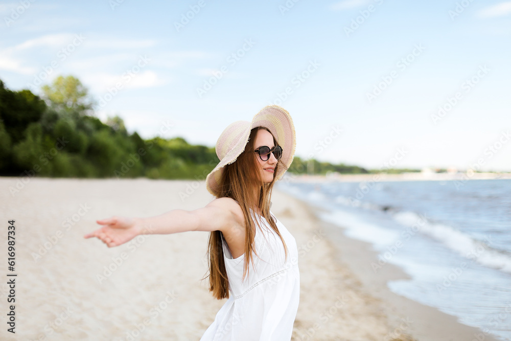 Happy smiling woman in free happiness bliss on ocean beach standing with a hat, sunglasses, and open hands. Portrait of a multicultural female model in white summer dress enjoying nature during travel Happy smiling woman in free happiness bliss on ocean beach standing with a hat, sunglasses, and open hands. Portrait of a multicultural female model in white summer dress enjoying nature during travel